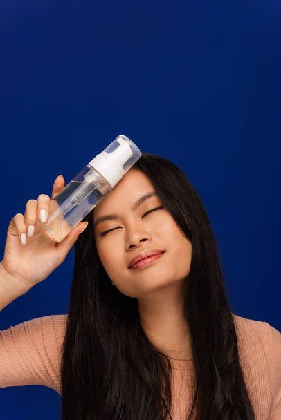 Pretty asian woman holding cleansing foam isolated on blue  - Fotografie, Obrázek