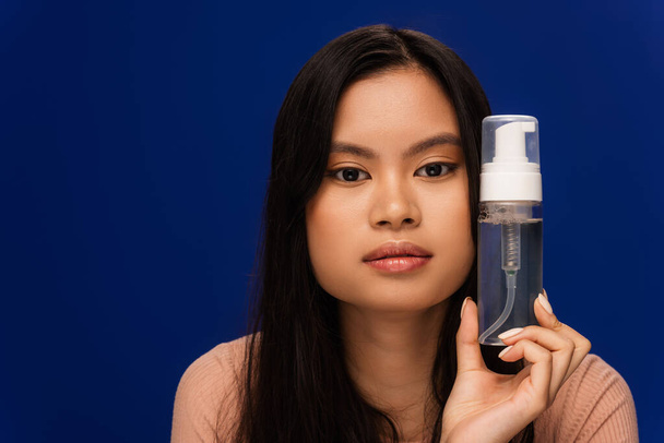 Портрет азійської жінки з ідеальною шкірою, що тримає піну на обличчі ізольованою на синьому  - Фото, зображення
