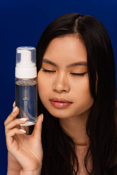 Pretty asian model with perfect skin holding face foam isolated on blue  - Fotoğraf, Görsel