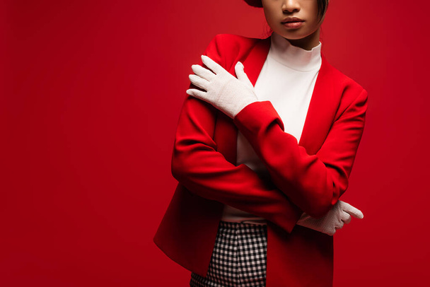 Обрізаний вид стильної жінки в піджаку і рукавичках позує ізольовано на червоному
  - Фото, зображення