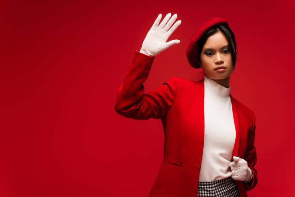 Asian woman in beret an gloves waving at camera isolated on red  - Fotografie, Obrázek