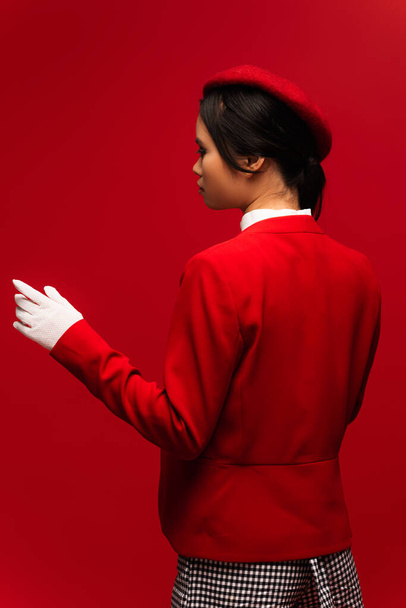 Side view of asian woman in beret nd blazer standing isolated on red  - Photo, Image