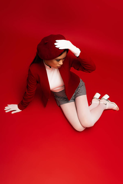 Overhead view of young asian model in stylish outfit sitting on red background  - Foto, Bild