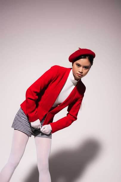 Pretty asian model in red jacket and plaid shorts posing on grey background  - Photo, image