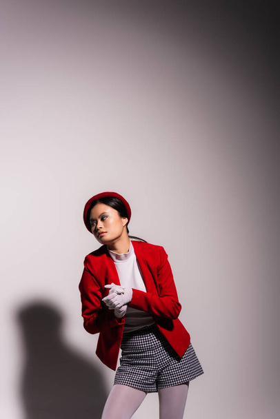 Young asian model in beret and jacket looking away on grey background  - Foto, afbeelding