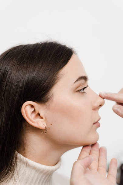 Rhinoplasty is reshaping nose surgery for change appearance of the nose and improve breathing. ENT doctor is touching nose and consulting girl patient in medical clinic before septoplasty surgery - Foto, imagen