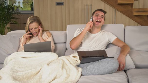 Busy couple having business calls while working remotely from home. Man and woman trying to do their work in living room while being isolated. Two adults using modern wireless devices. - Φωτογραφία, εικόνα