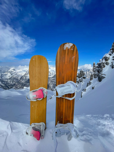 Two snowboards stuck in pile of snow on top of freeride line with fresh snowpack. Female and male snowboard setup in full readiness for riding powder snow on untouched and pristine mountain terrains. - Foto, afbeelding