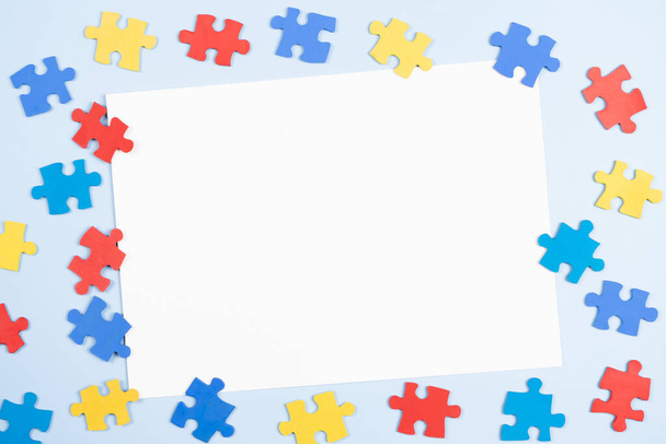 Blank white paper card with blue, yellow, red pieces of puzzle on light blue frame background. World autism awareness day concept. Top view, copy space. - Fotoğraf, Görsel