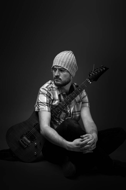 charismatic guy sitting in thought with an electric guitar, black and white artistic photo - Foto, afbeelding