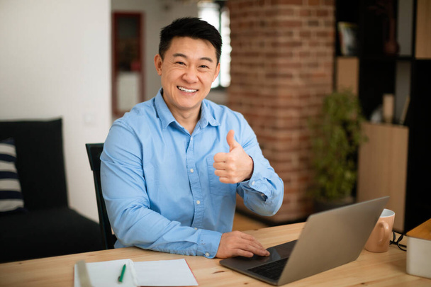I like it. Happy middle aged asian businessman sitting at desk, using laptop and showing thumb up, working at home office and smiling at camera, free space - Fotografie, Obrázek