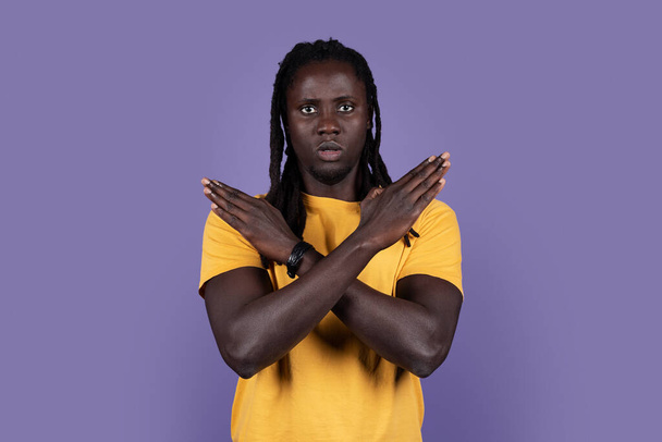 Serious african american millennial guy in casual saying no, looking at camera and showing hands crossed over chest, purple studio background, copy space. Human gestures, cross sign concept - Foto, afbeelding