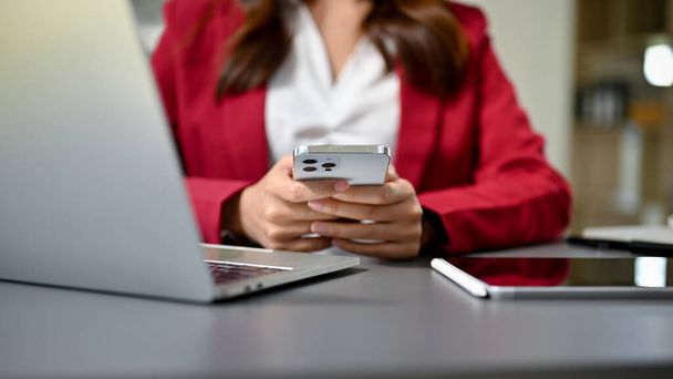 Красивая деловая женщина или женщина-босс, используя свой смартфон за столом, смс или отправка электронной почты, проверка графика встреч, поиск информации в Интернете. обрезанное изображение - Фото, изображение