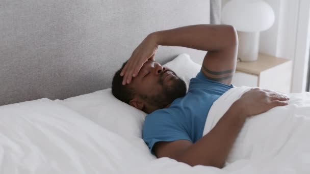Bad sleep problem. Young african american guy waking up in bed and massaging forehead, suffering from headache and keep resting, tracking shot, slow motion, empty space - Video, Çekim