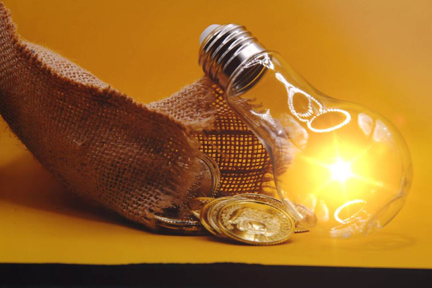 Rising energy cost concept. Light bulb on top of a stack of gold coins . - Zdjęcie, obraz