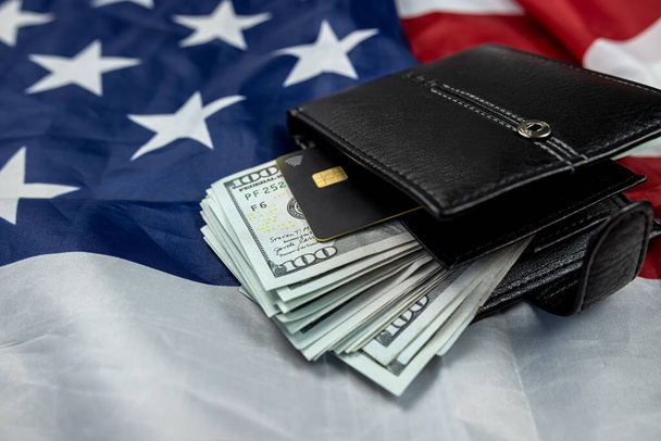 Δερμάτινο πορτοφόλι με χαρτονομίσματα των εκατό δολαρίων που απομονώνονται στο φόντο της σημαίας των ΗΠΑ. ευημερία της χώρας. σύμβολο του πλούτου. - Φωτογραφία, εικόνα