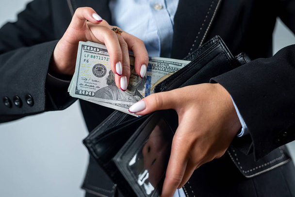 close-up of a female hand holding a black wallet in which there are dollars. woman with dollars money in wallet abundance - Photo, Image