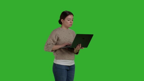 Вид збоку впевнена дівчина прокручує через інтернет на ноутбуці, працюючи з портативним ПК над ізольованим зеленим фоном екрану. Сучасна жінка використовує бездротовий комп'ютер та онлайн додаток соціальних мереж
. - Кадри, відео
