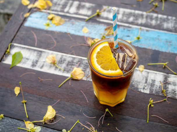 Склянка свіжого оранжевого американця, прикрашена нарізаним апельсином, подається на дерев'яному столі, вид зверху. Холодна чорна кава з апельсиновим соком, змішування меню з макаронами
. - Фото, зображення