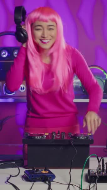 Vertical video: Asian performer mixing stereo sounds with electronics, standing at dj table performing remix using professional mixer console. Cheerful artist enjoying playing music in nightxlub - Záběry, video