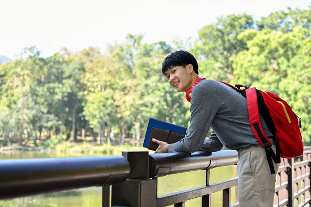 Щасливий і холодний молодий азіат-студент коледжу відпочиває в університетському парку з прекрасним ставок. Концепція способу життя - Фото, зображення