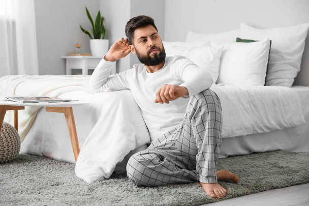Задумчивый молодой бородатый мужчина сидит дома на ковре - Фото, изображение