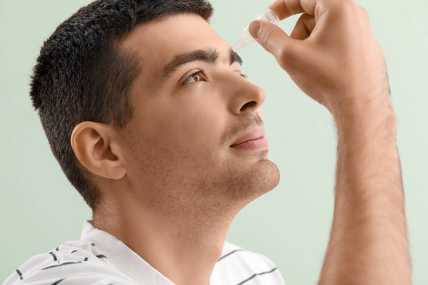 Young man using eye drops on green background, closeup - Photo, image