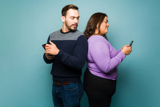 Järkyttynyt valkoihoinen mies vakoilee hänen latina tyttöystävä tekstailee toinen mies älypuhelimeen samalla huijaaminen  - Valokuva, kuva