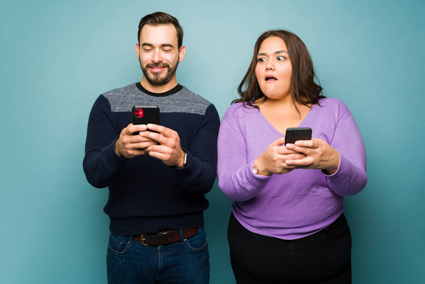 Järkyttynyt lihava nainen vakoilee hänen pettäminen onnellinen poikaystävä taas tekstaamalla toinen nainen älypuhelimeen - Valokuva, kuva