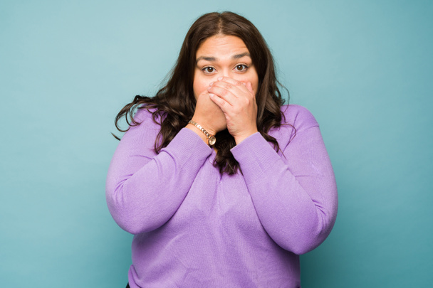 Shocked fat young woman covering her mouth and looking sick suffering from bad breath - Fotó, kép