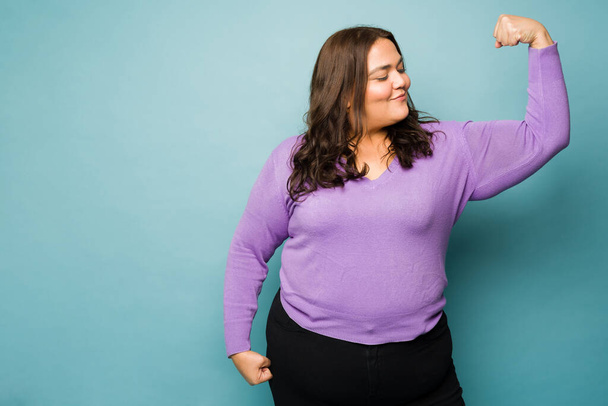 Powerful overweight young woman doing a bicep curl feeling strong promoting girl power and body positivity - Fotó, kép