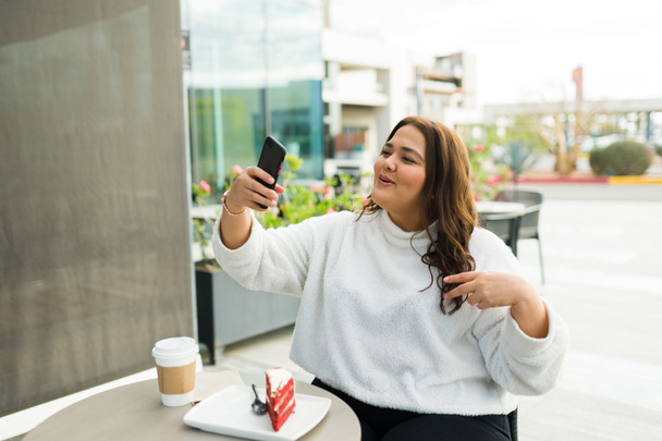 Attractive fat woman working as a content creator filming a social media story with her smartphone while at the coffee shop - Foto, Imagen