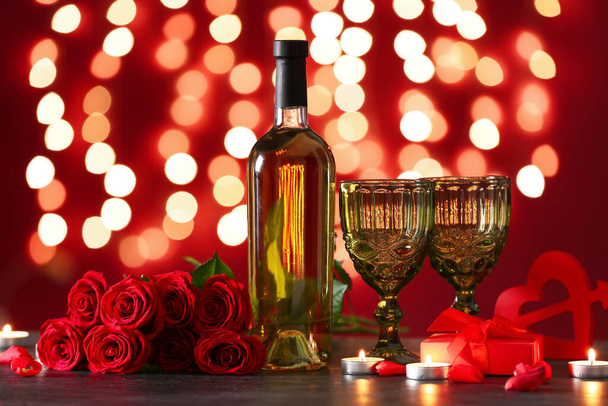 Μπουκάλι κρασί, τριαντάφυλλο λουλούδια, ποτήρια και αναμμένα κεριά σε μαύρο τραπέζι ενάντια στα θολά φώτα. Γιορτή του Αγίου Βαλεντίνου - Φωτογραφία, εικόνα