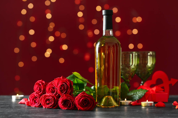 Μπουκάλι κρασί, τριαντάφυλλο λουλούδια και αναμμένα κεριά σε μαύρο τραπέζι κατά θολή φώτα. Γιορτή του Αγίου Βαλεντίνου - Φωτογραφία, εικόνα