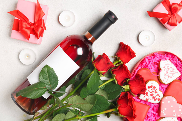 Μπουκάλι κρασί, τριαντάφυλλο λουλούδια, κουτιά δώρων και μπισκότα σε σχήμα καρδιάς σε λευκό τραπέζι. Γιορτή του Αγίου Βαλεντίνου - Φωτογραφία, εικόνα
