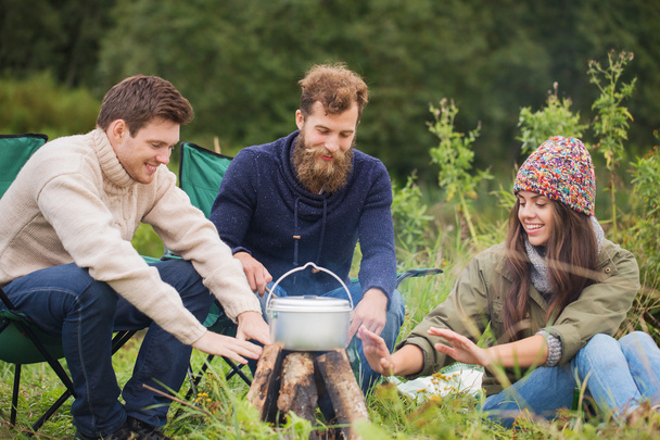 group of smiling friends cooking food outdoors - Photo, Image
