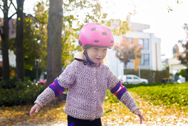 Smiling child girl in a helmet in protection rollerblades in the park. - Foto, imagen