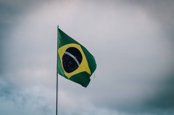 Σημαία Βραζιλίας κυματίζει σε ένα στύλο με συννεφιά ουρανό. - Φωτογραφία, εικόνα