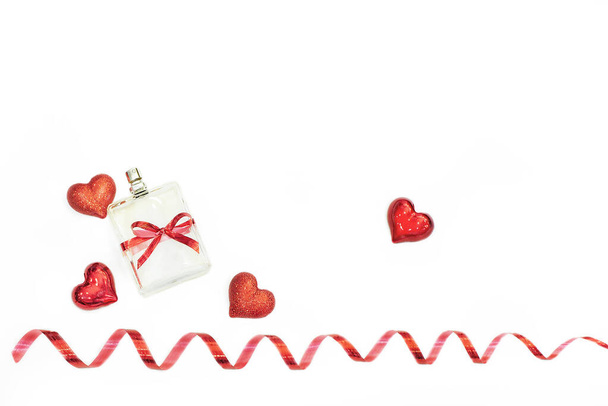 perfume bottle tied with a red festive ribbon among red hearts and ribbon on a white background.Gift card for valentines day,closeup,place for text,copyspace.Presentation of cometics as a gift,mockup - Foto, afbeelding
