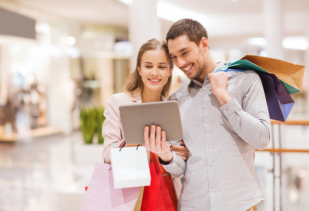 couple with tablet pc and shopping bags in mall - Photo, image