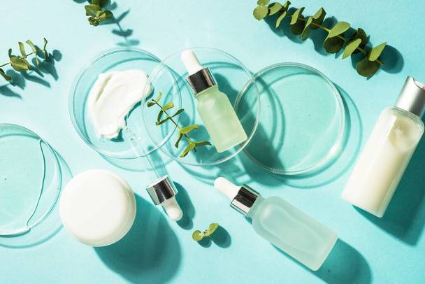 Concepto de laboratorio cosmético. Placa Petri de vidrio con productos cosméticos y botellas de suero en fondo azul. Imagen de laico plano. - Foto, Imagen