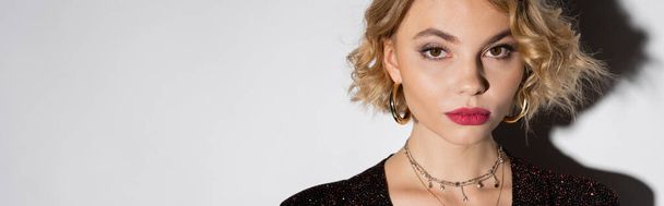 portrait of blonde young woman in golden hoop earrings and silver necklace looking at camera on white, banner  - Foto, Imagem