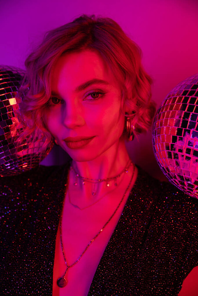 young woman with blonde hair near shiny disco balls on purple and pink  - Foto, immagini