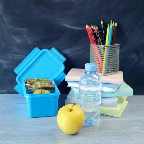 Lunchbox with sandwich, water bottle, apple, books and stationery on wooden table, chalkboard background, back to school  - Foto, Imagen