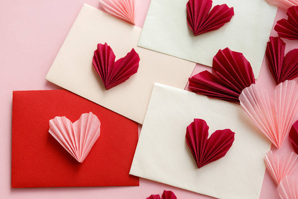 С Днем Святого Валентина! Стильные конверты с плоскими розовыми и красными сердцами лежат на розовом бумажном фоне. Творческая современная валентинка сердца вырезает композицию. Любовное письмо - Фото, изображение
