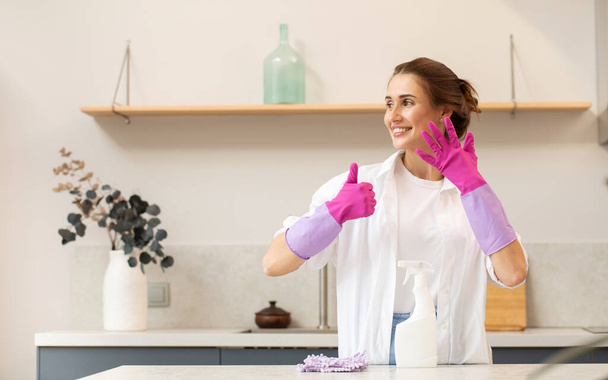 Attractive housewife holds a spray bottle with cleaning agent in her hand and shows a thumbs up. The concept of home cleaning, cleaning service. - Foto, immagini