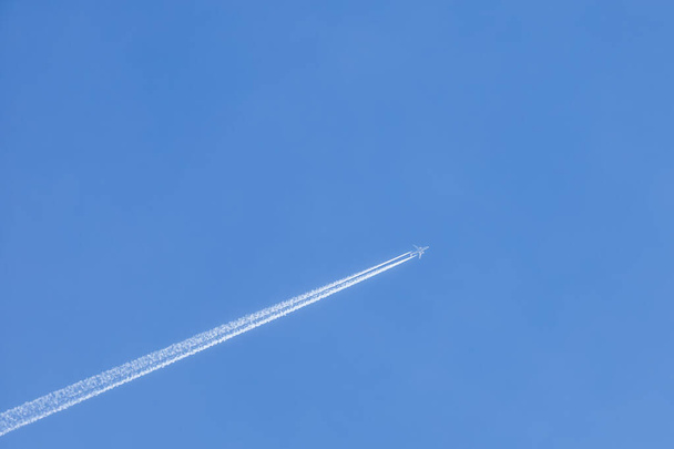 A large airliner in a cloudless blue sky. There is a long trail behind the plane. - Photo, image