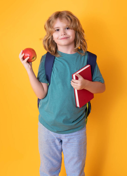 Малюк зі школи. Шкільна дитина в шкільній формі з книгою сумки та яблуком. Шкільні діти на студії ізольовані жовтий фон
 - Фото, зображення