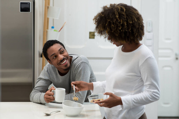 Happy african american young couple have breakfast together at home, handsome man drink fresh aromatic coffee, curly woman making granola, lovers having conversation. Family, marriage, relationships - Foto, Imagem