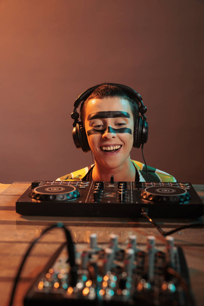 Young performer looking at dj turntables in studio, preparing to mix techno music and have fun at nightclub. Woman with crazy make up watching mixer on table, look closely and acting silly. - Foto, Imagen